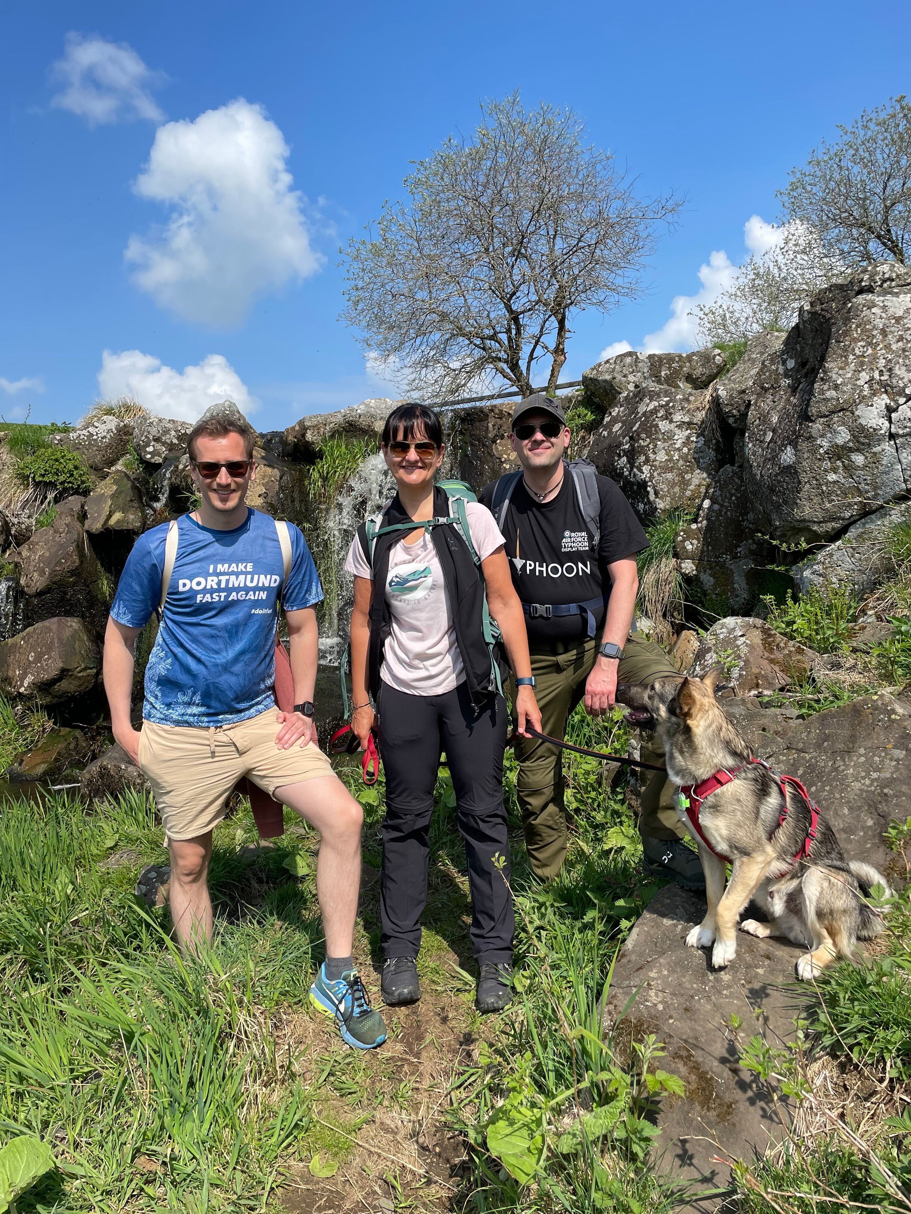 Drei Personen und ein Hund bei einem Zwischenstopp auf einem Berg beim Wandern.