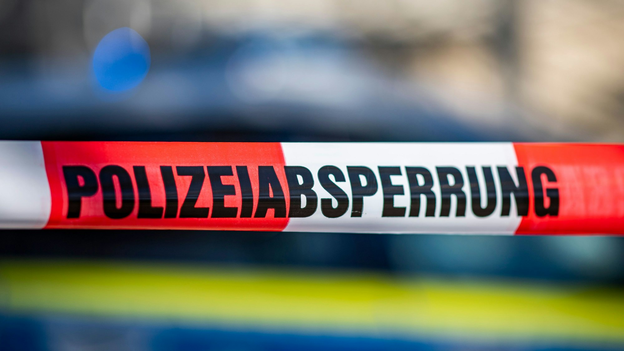 Ein Absperrband mit der Aufschrift „Polizeiabsperrung“ ist vor einem Polizeiwagen aufgespannt.