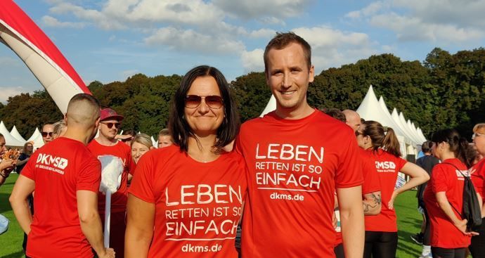 Eine Frau und ein Mann in roten Shirts halten sich im Arm und posieren für die Kamera.