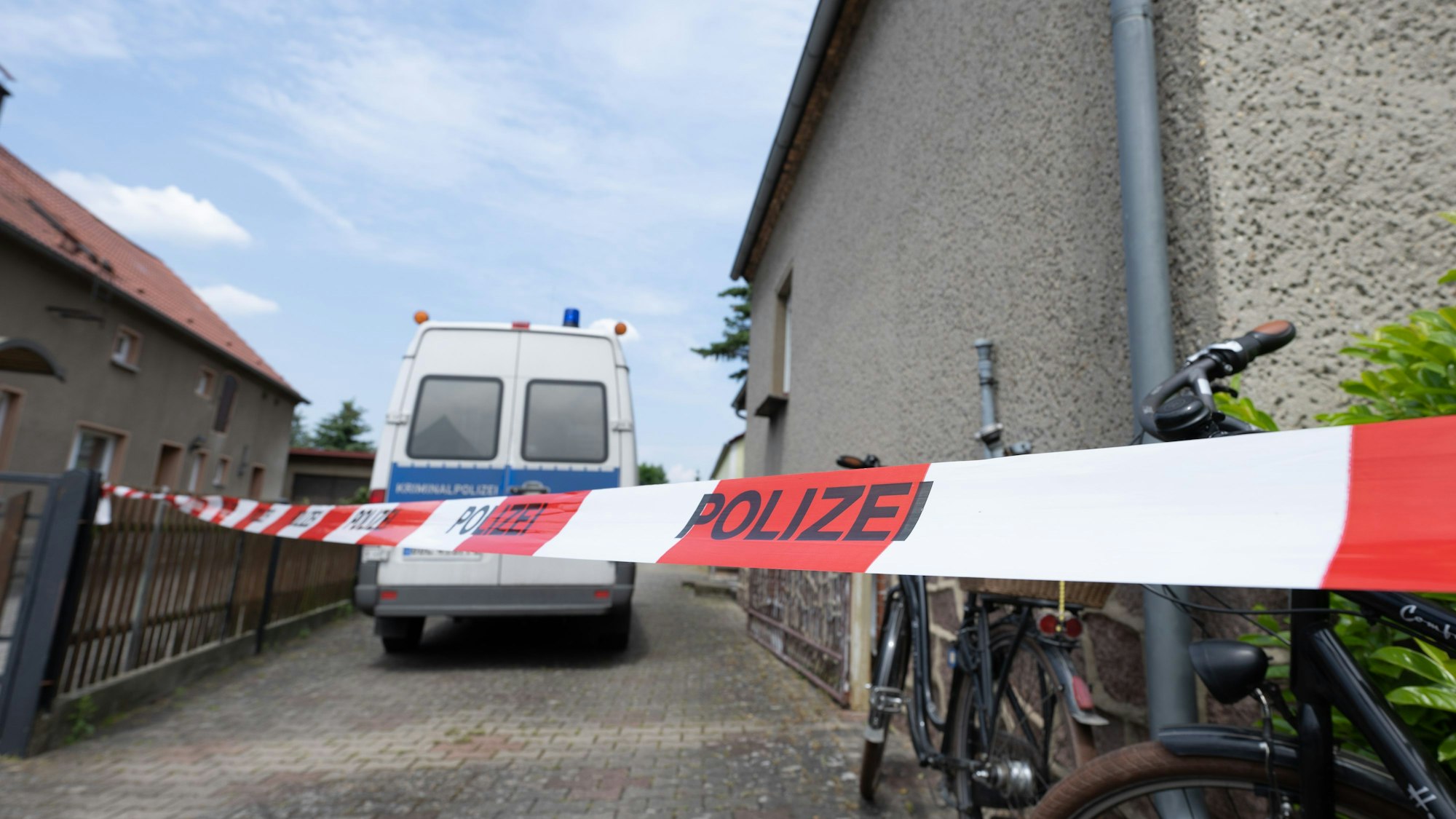 Ein Fahrzeug der Polizei steht in einer Hauszufahrt, die mit einem Flatterband abgesperrt ist.