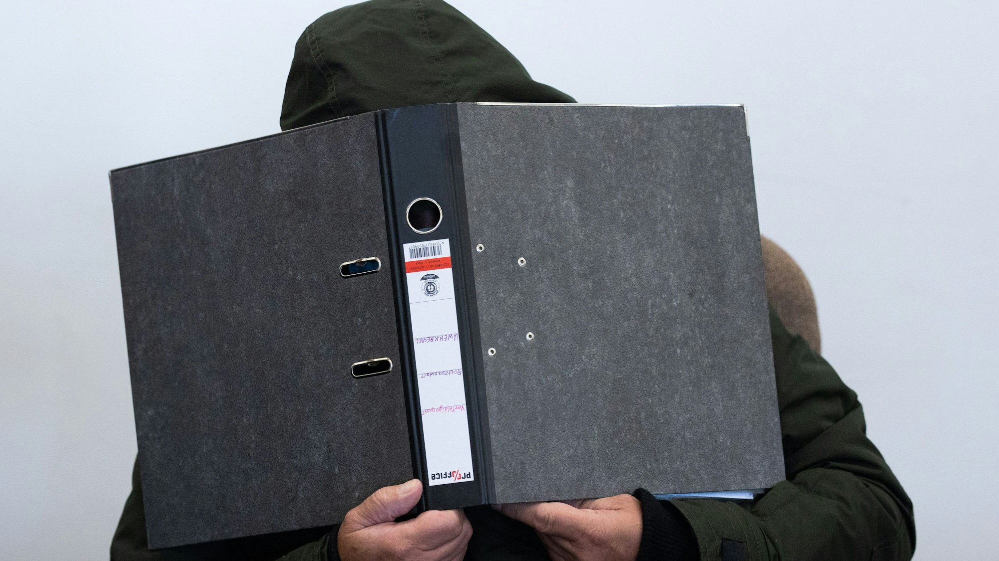 Der Angeklagte verdeckt mit einem Aktenordner sein Gesicht. Seit dem 4. September 2023 läuft im Landgericht Köln der Mordprozess im sogenannten Karnevalsmord.