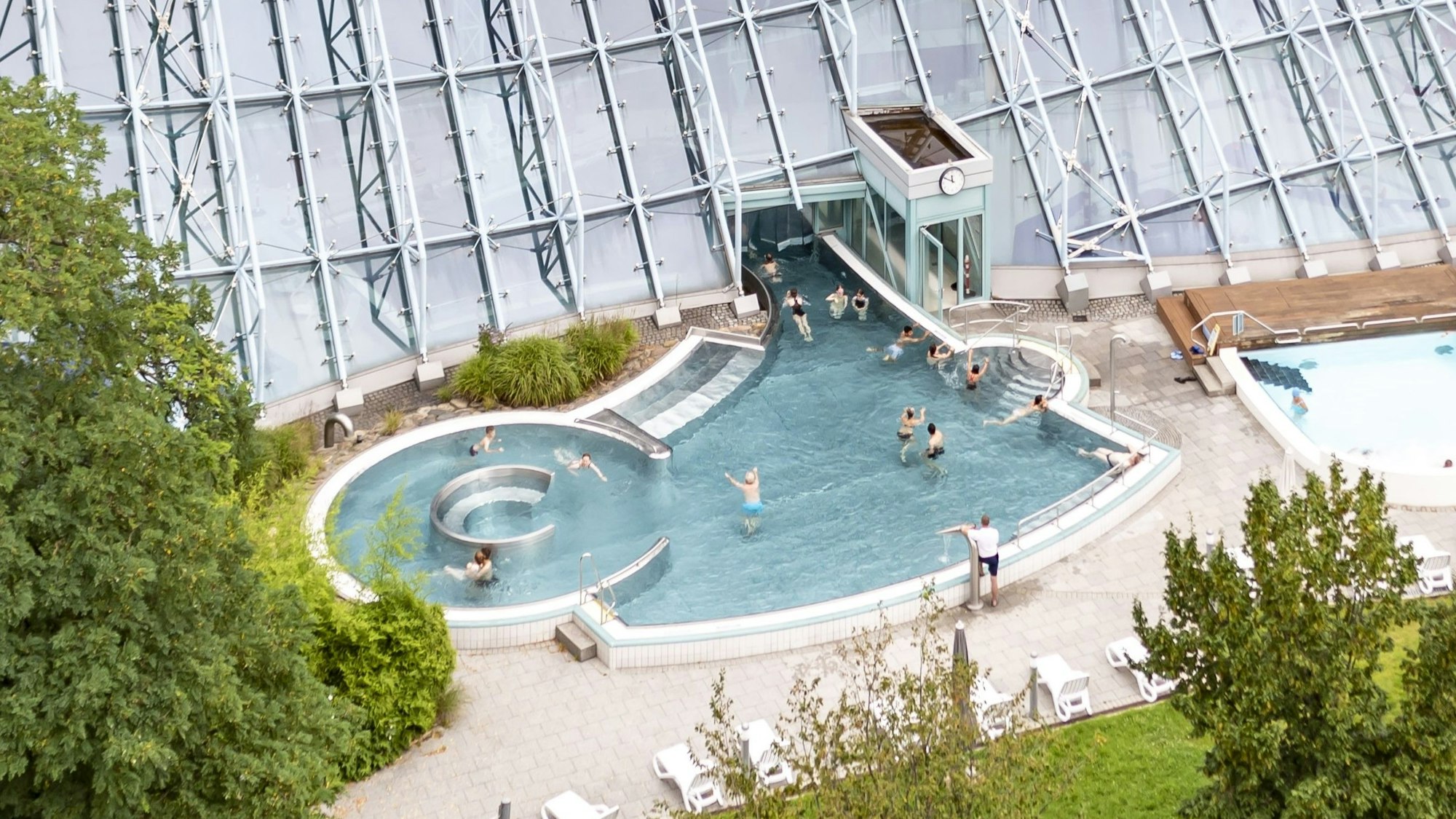In einem Außenbecken eines Schwimmbads tummeln sich zahlreiche Menschen.