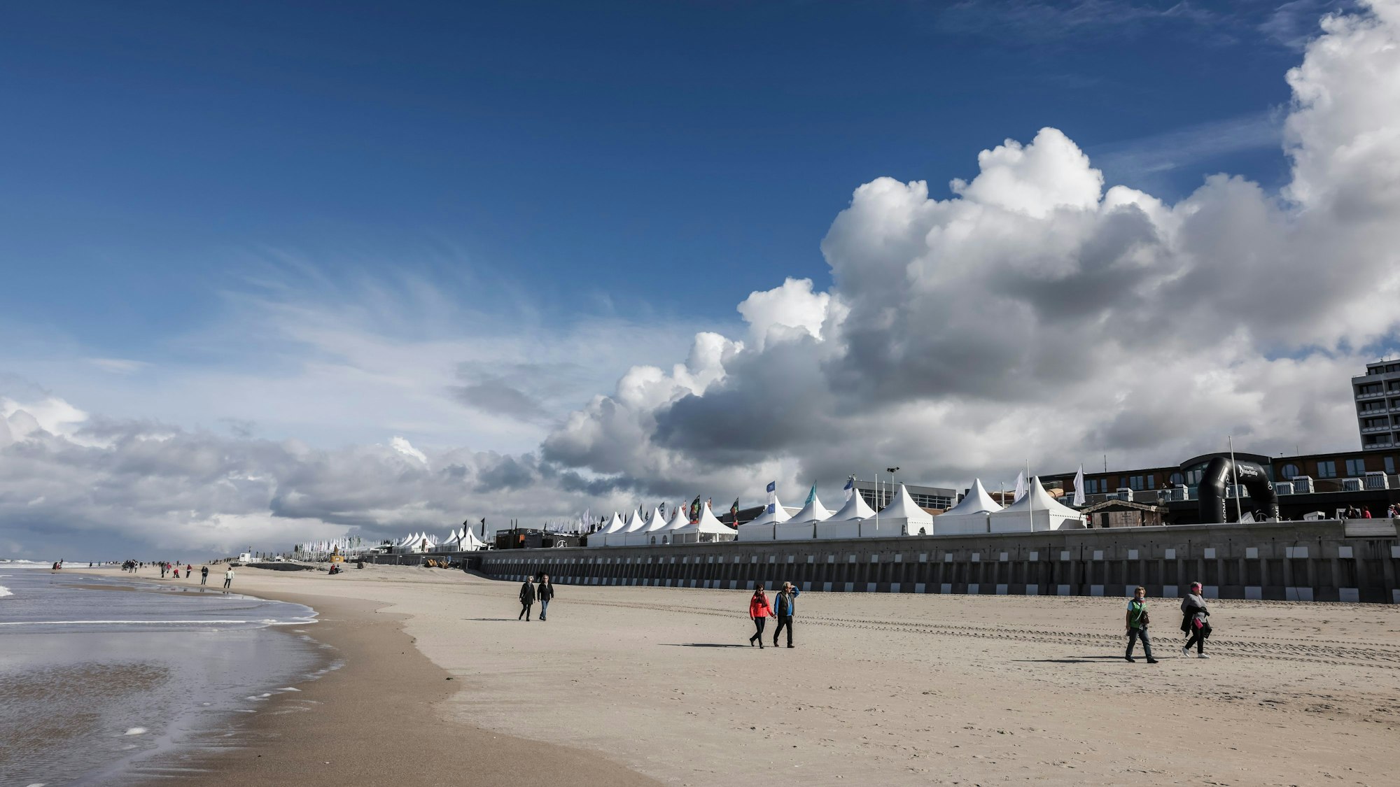 Spaziergänger und Spaziergängerinnen gehen bei Sonnenschein am Brandenburger Strand spazieren.