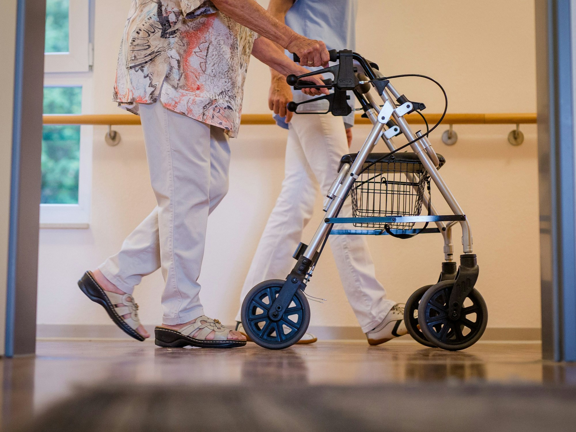 Eine Pflegekraft geht in einem Pflegeheim mit einer älteren Dame über einen Korridor.