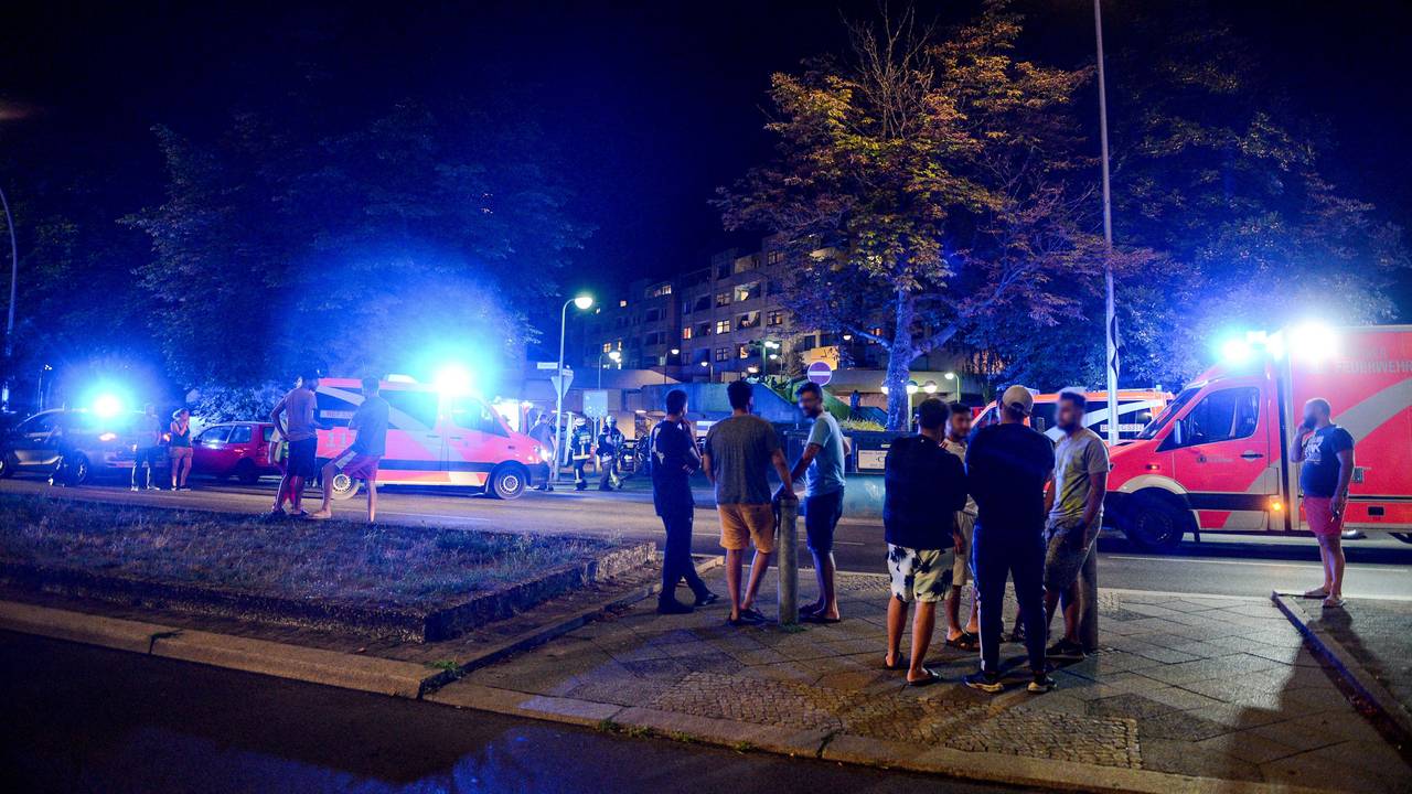 Feuerwehr und Rettungskräfte sind im Zuge eines Kellerbrandes am 08.08.2018 im Einsatz, während sich Anwohnerinnen und Anwohner auf der Straße vor dem Gebäude aufhalten.