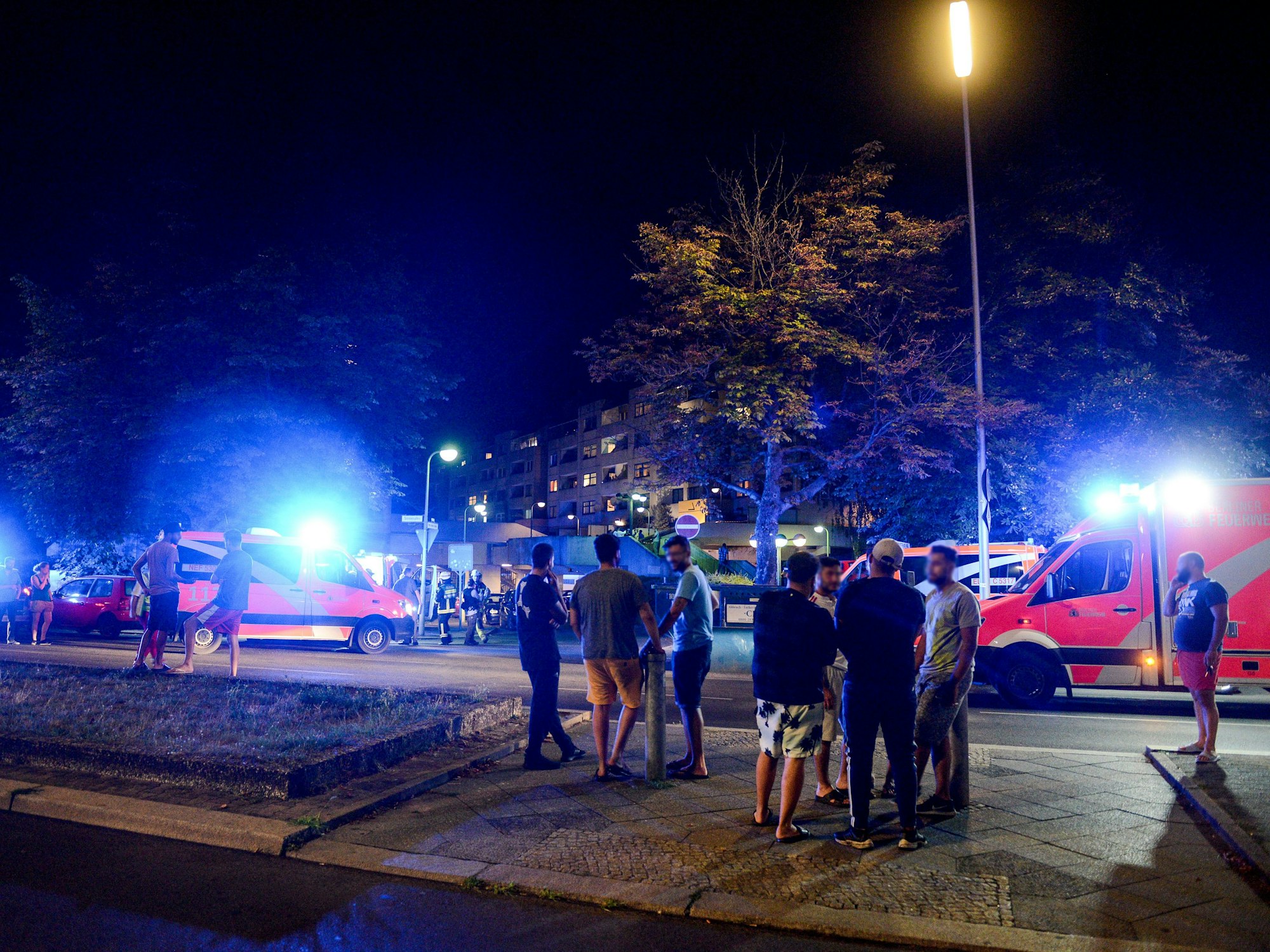 Feuerwehr und Rettungskräfte sind im Zuge eines Kellerbrandes am 08.08.2018 im Einsatz, während sich Anwohnerinnen und Anwohner auf der Straße vor dem Gebäude aufhalten.