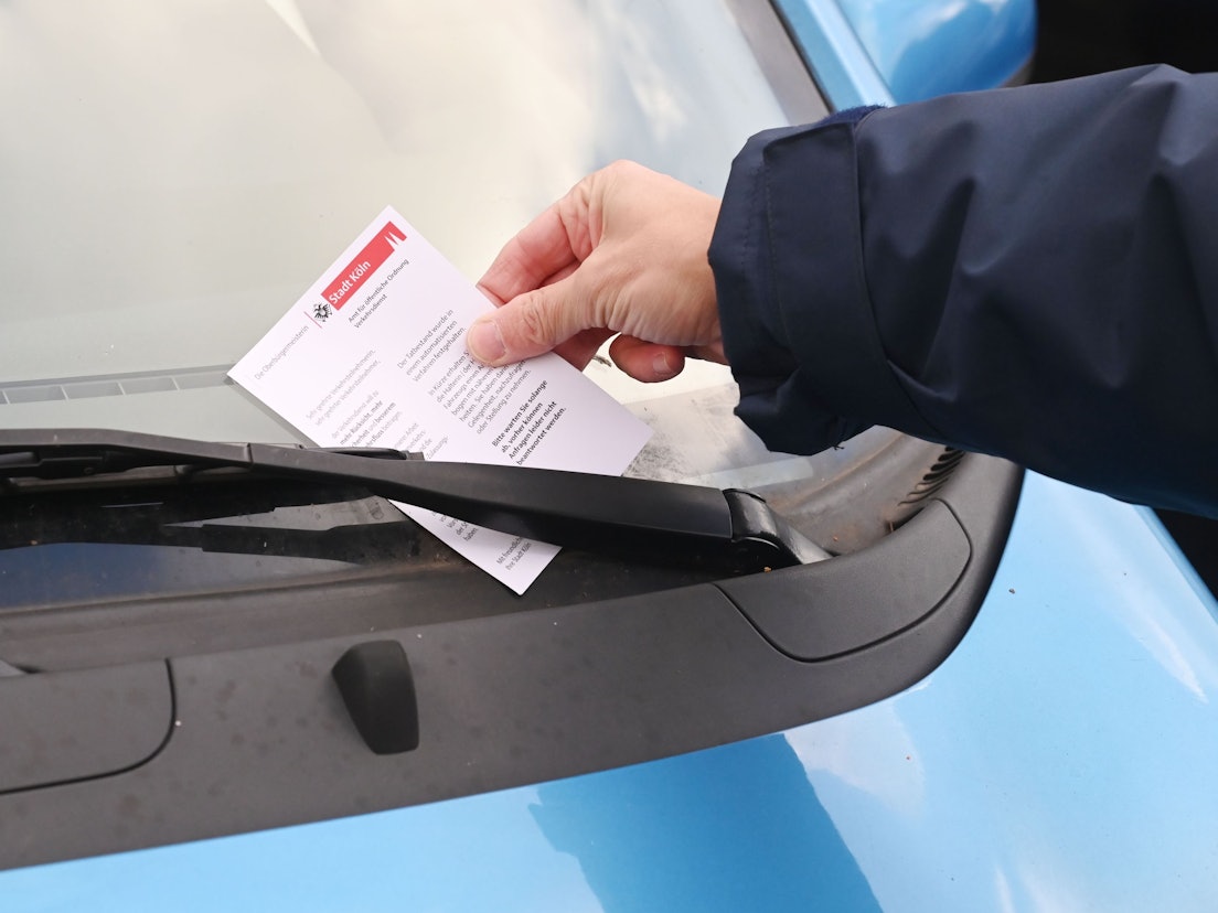 Ein Mitarbeiter des Ordnungsamtes steckt ein Knöllchen hinter einen Scheibenwischer.