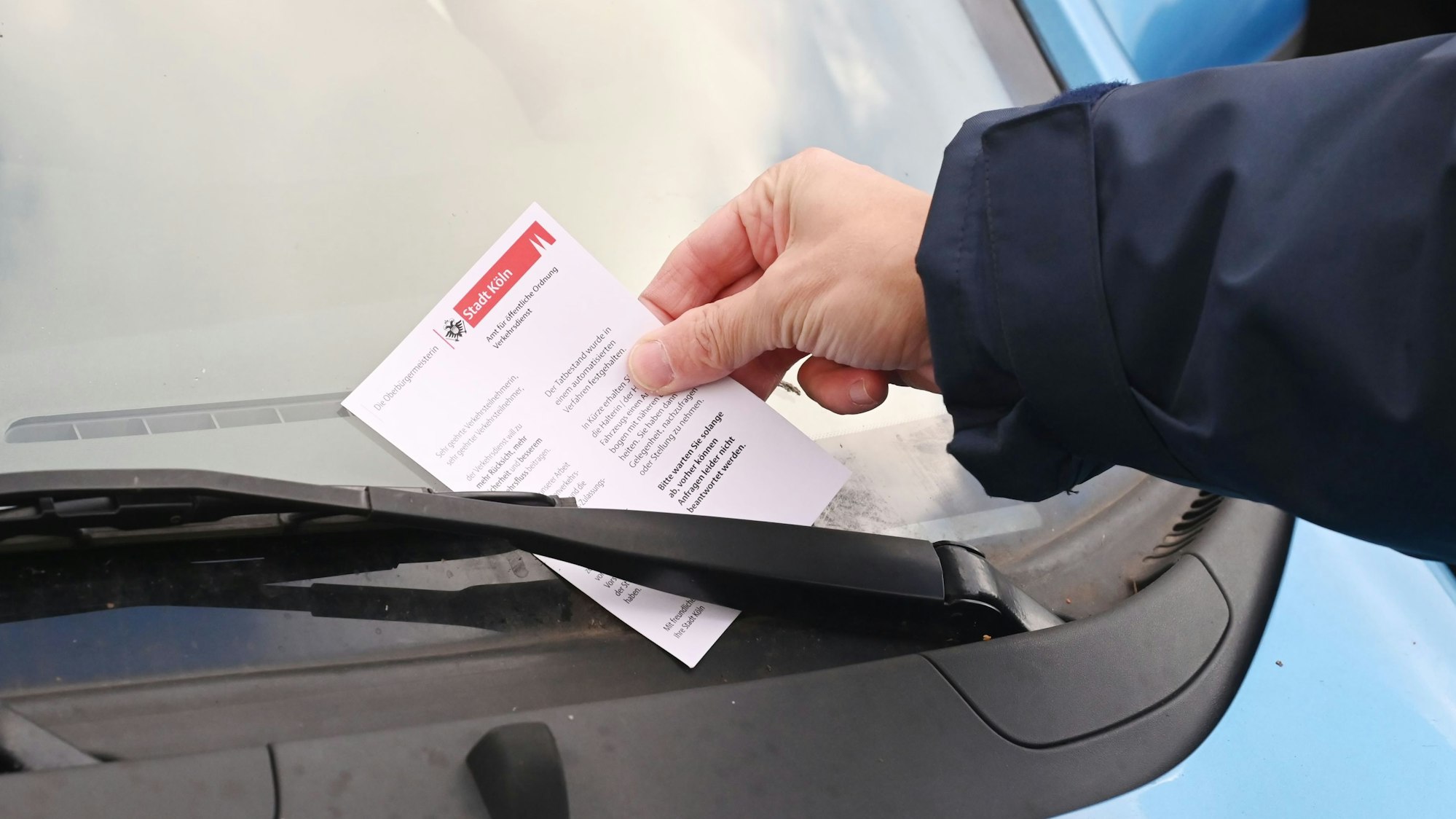 Ein Mitarbeiter des Ordnungsamtes steckt ein Knöllchen hinter einen Scheibenwischer.