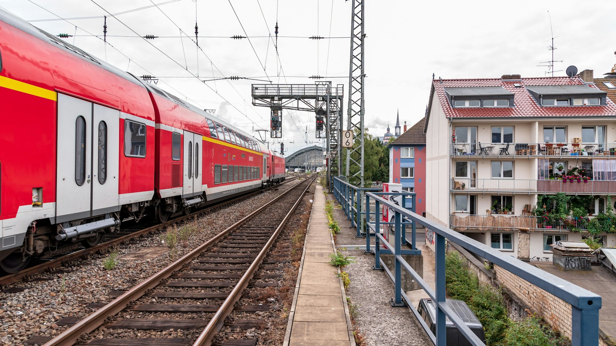 Ein Regionalexpress der Deutschen Bahn fährt über die Gleise an einem Wohngebiet in Köln vorbei.