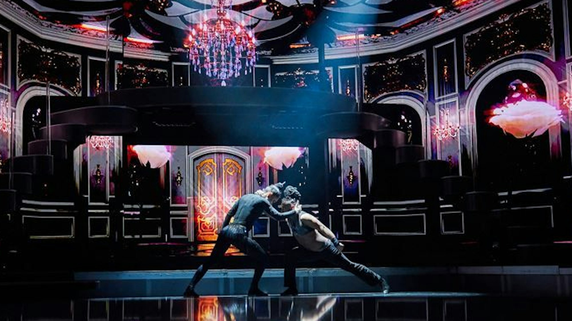 Zwei Menschen tanzen gemeinsam auf einer dunklen Bühne.