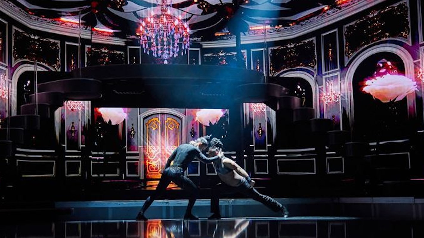 Zwei Menschen tanzen gemeinsam auf einer dunklen Bühne.