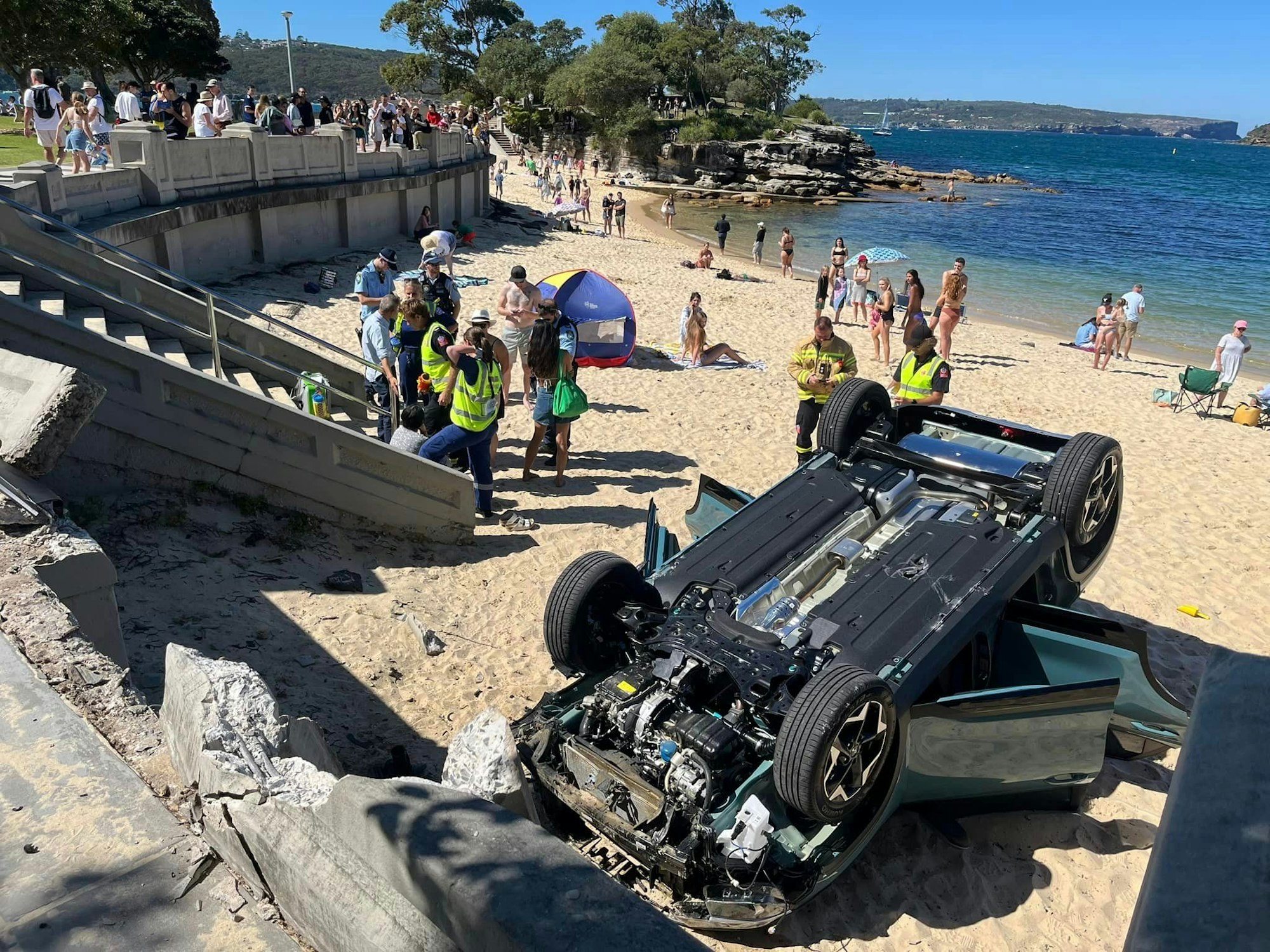 Ein Auto liegt auf dem Dach am Strand von Balmoral Beach. Eine australische Fahranfängerin wollte in Sydney das Einparken üben – und ist mit ihrem Auto mit voller Wucht auf einem belebten Strand gelandet.