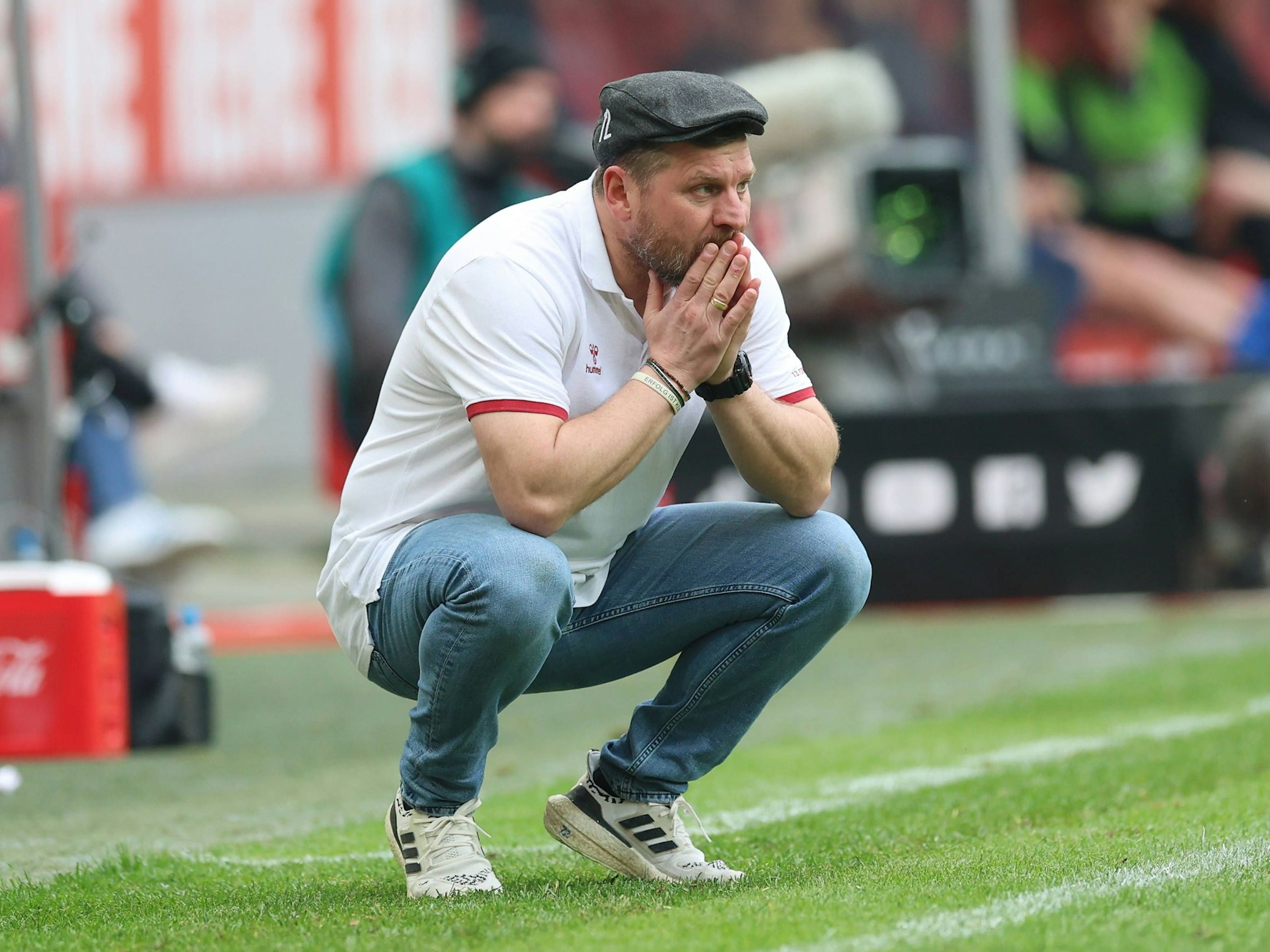 Steffen Baumgart ist in der Hocke und hält die Hände vor seinen Mund.