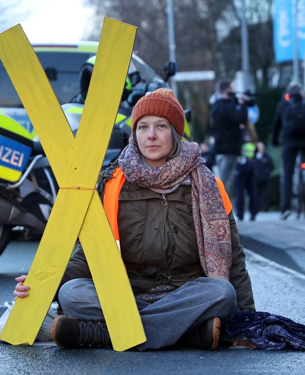 Eine Frau sitzt auf der Fahrbahn und hält ein großes X aus Pappe fest.