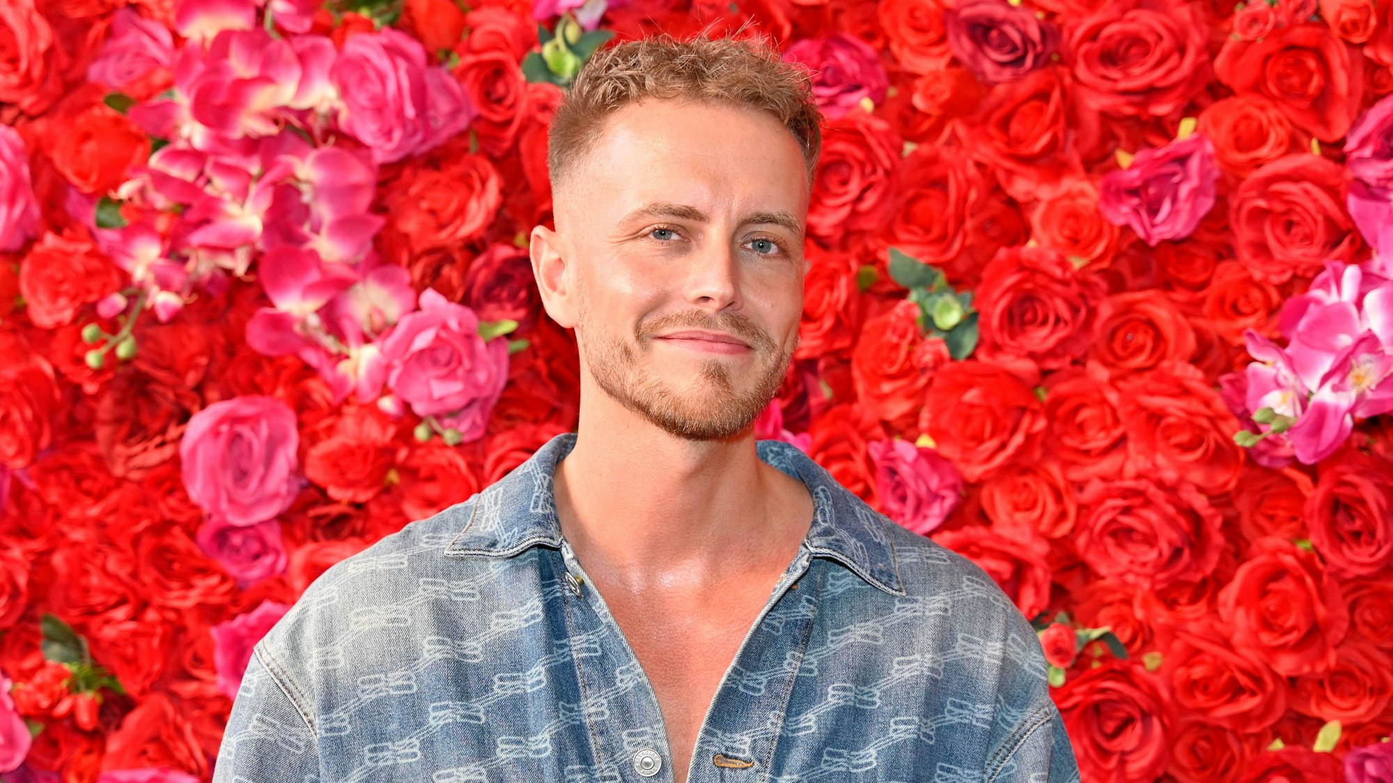 Das Foto zeigt Julian Claßen bei der Eröffnung des TKMaxx-Shops im Supercandy Pop-Up Museum in Köln vor einer Wand aus Rosen.