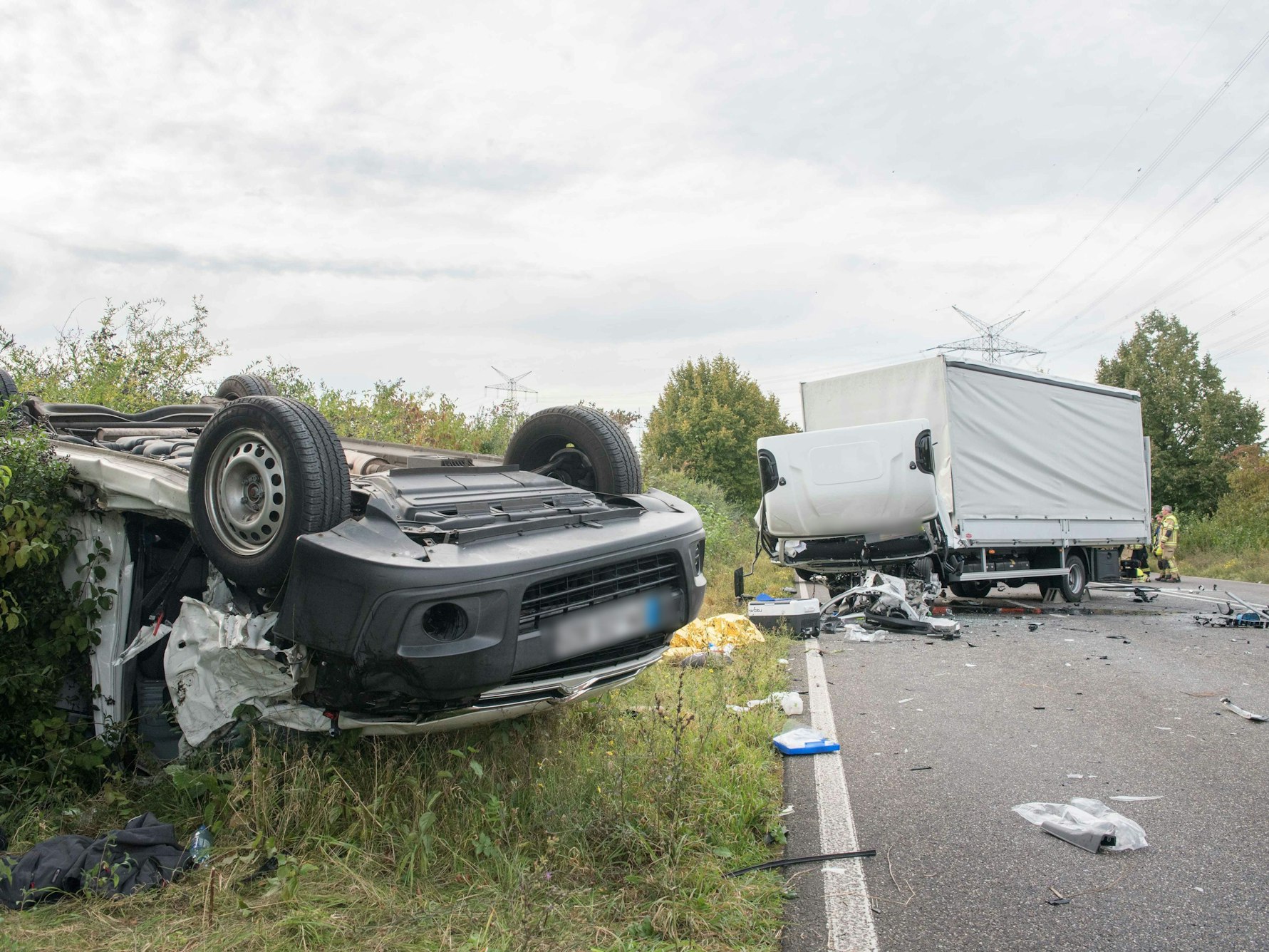 Nach einem Verkehrsunfall steht ein völlig zerstörter Lkw auf der Fahrbahn, am Straßenrand liegt ein weiteres Fahrzeug auf dem Dach.