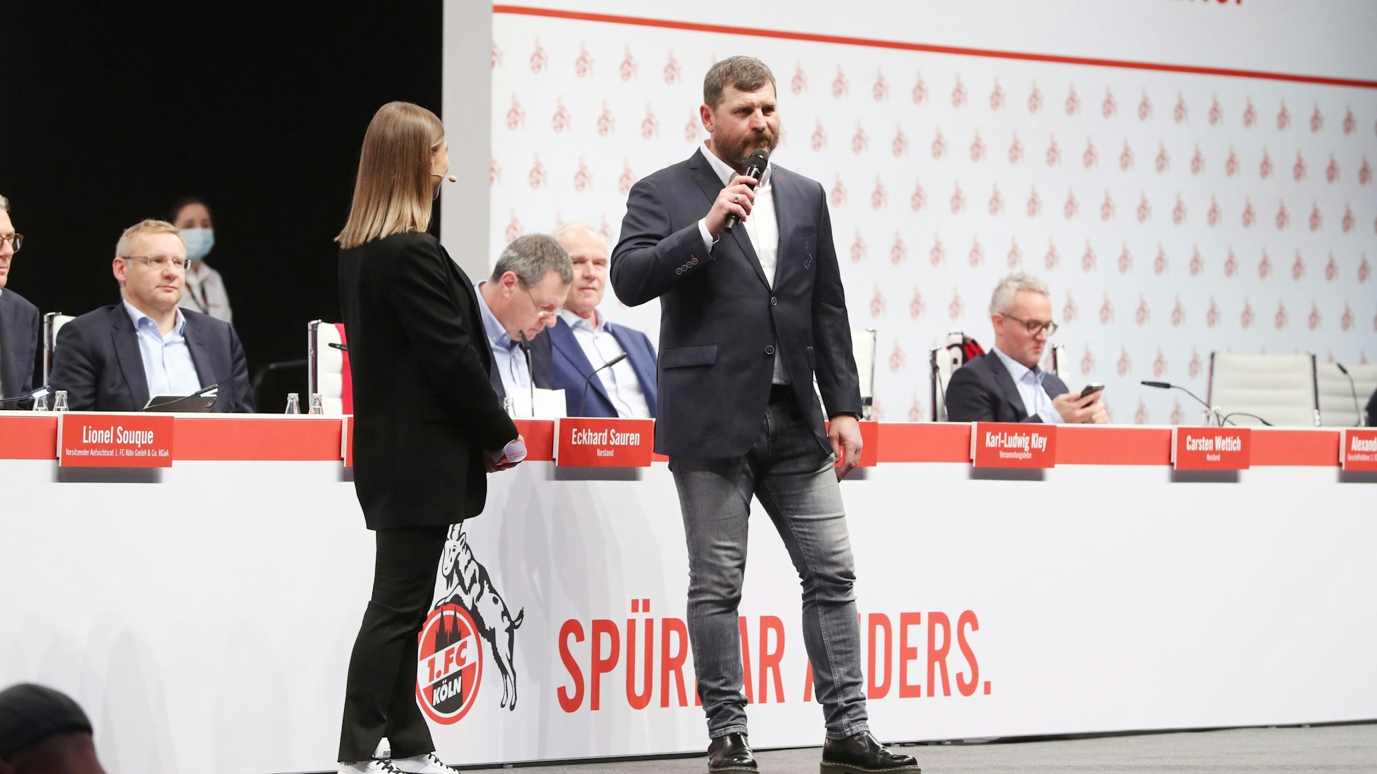 Steffen Baumgart steht bei der Mitgliederversammlung des 1. FC Köln mit dem Mikrofon auf der Bühne.