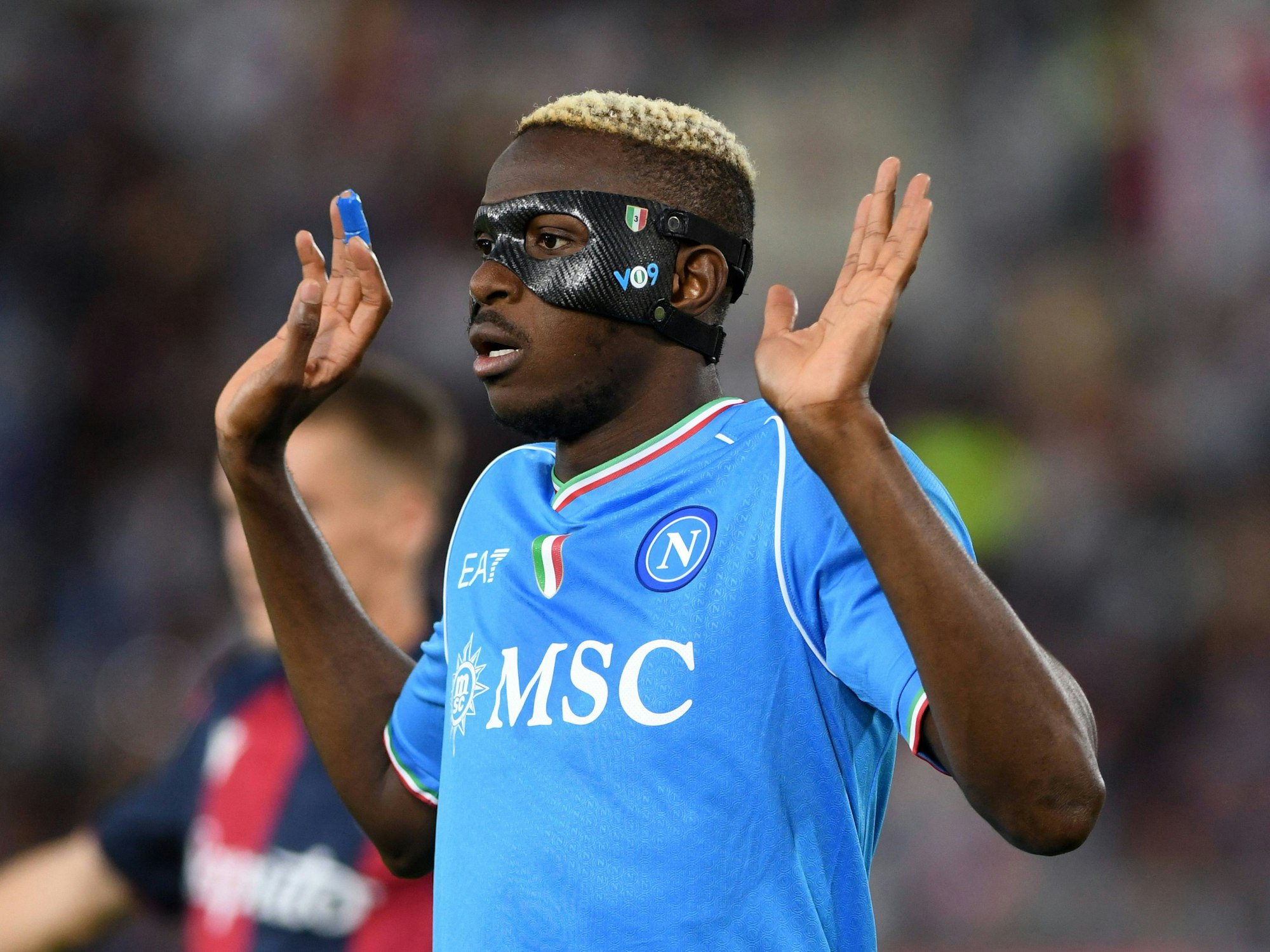 Victor Osimhen, der eine Gesichtsmaske zum Schutz trägt, hebt die Hände.