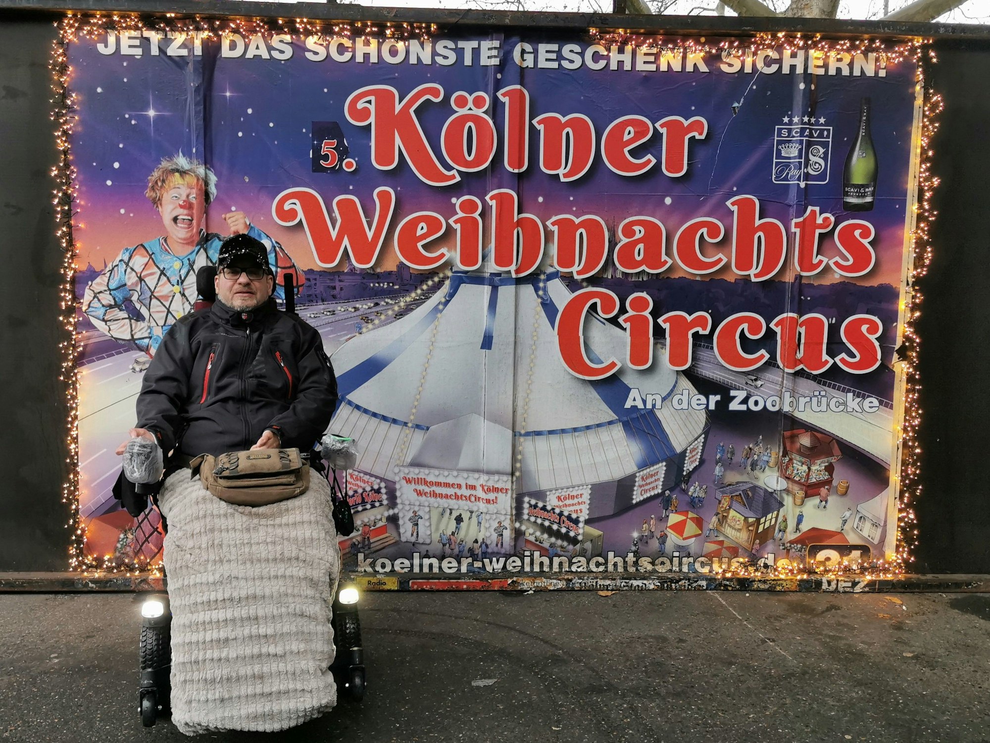 Rollstuhlfahrer Dirk posiert vor einem Werbeplakat des Weihnachtscircus