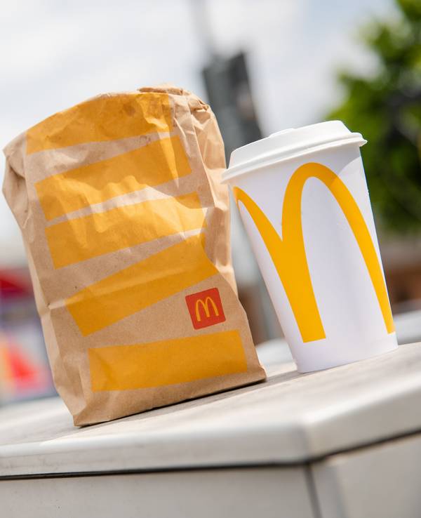 Eine McDonald's To-Go-Tüte und ein dazugehöriger To-Go-Becher stehen vor einer Tübinger McDonald's Filiale.