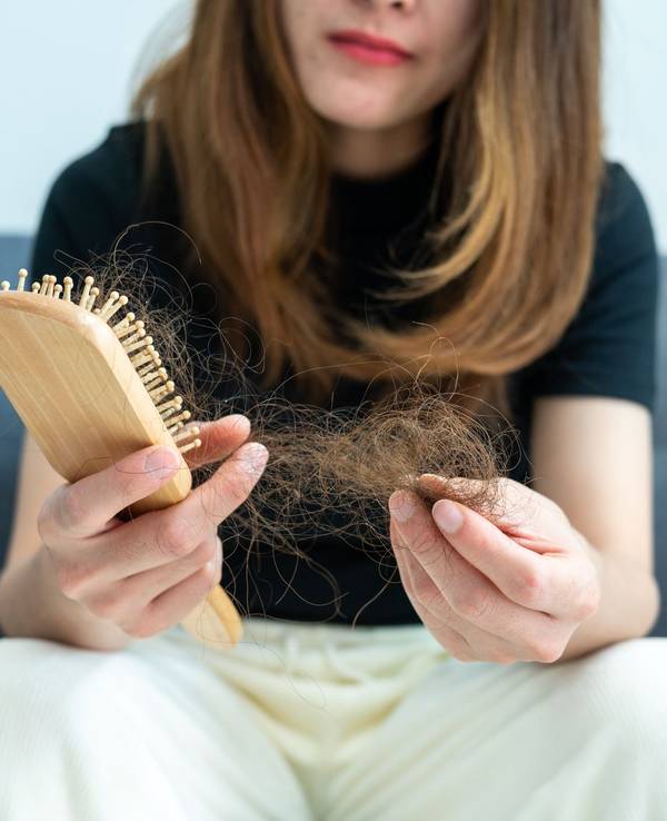 Eine Frau zieht verlorene Haare aus einer Haarbürste.