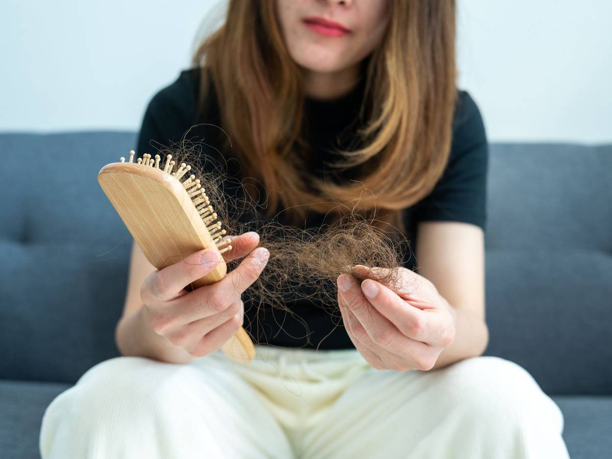Eine Frau zieht verlorene Haare aus einer Haarbürste.