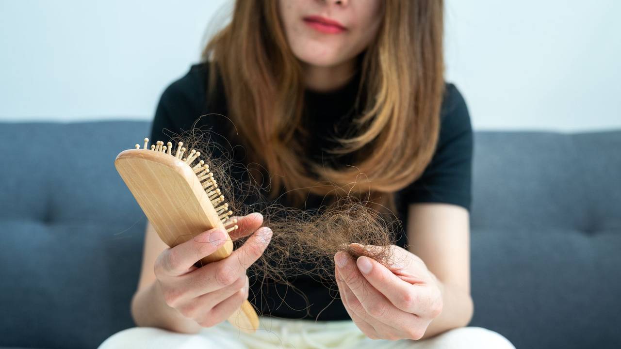 Eine Frau zieht verlorene Haare aus einer Haarbürste.