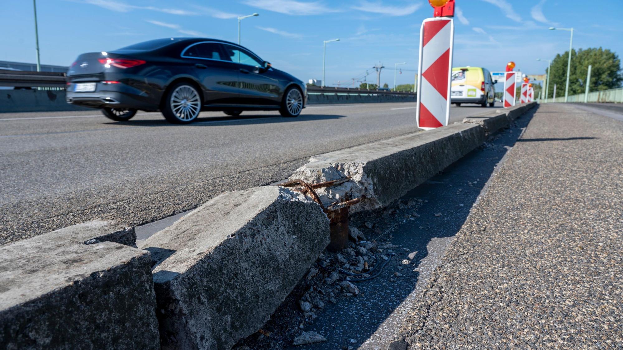 Ein Bordstein auf der Zoobrücke in Köln ist gebrochen. Im Hintergrund fahren Autos.