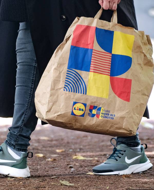 Ein Lidl-Kunde läuft mit einer Einkaufstasche des Discounters in Düsseldorf über die Straße.