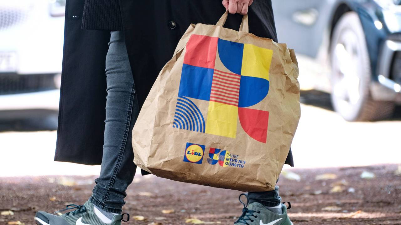 Ein Lidl-Kunde läuft mit einer Einkaufstasche des Discounters in Düsseldorf über die Straße.