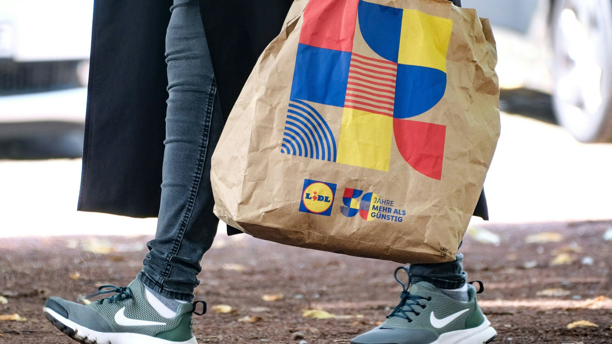 Ein Lidl-Kunde läuft mit einer Einkaufstasche des Discounters in Düsseldorf über die Straße.