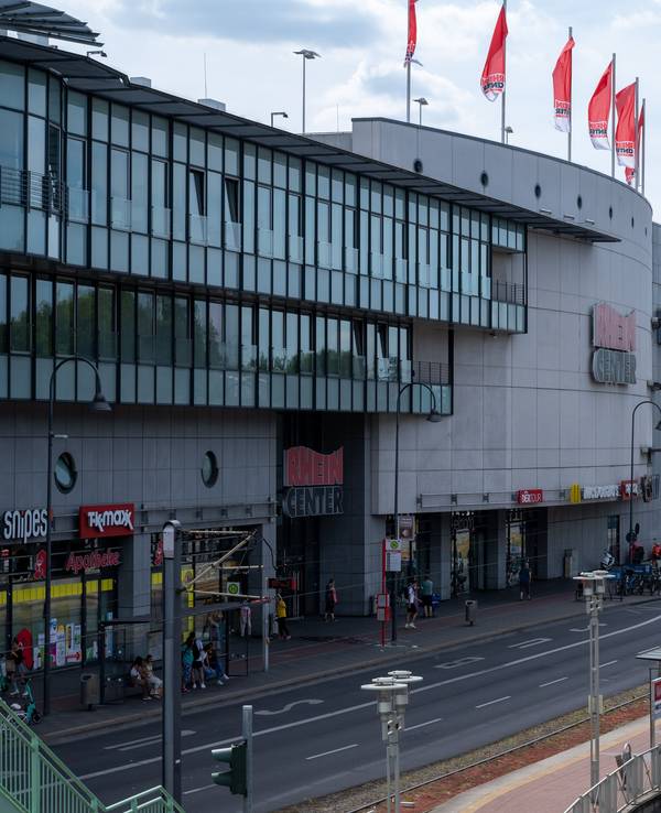 Blick auf das Einkaufszentrum Rhein-Center in Weiden. Im Vordergrund ist der Straßenverkehr mit Autos und Bussen zu sehen.