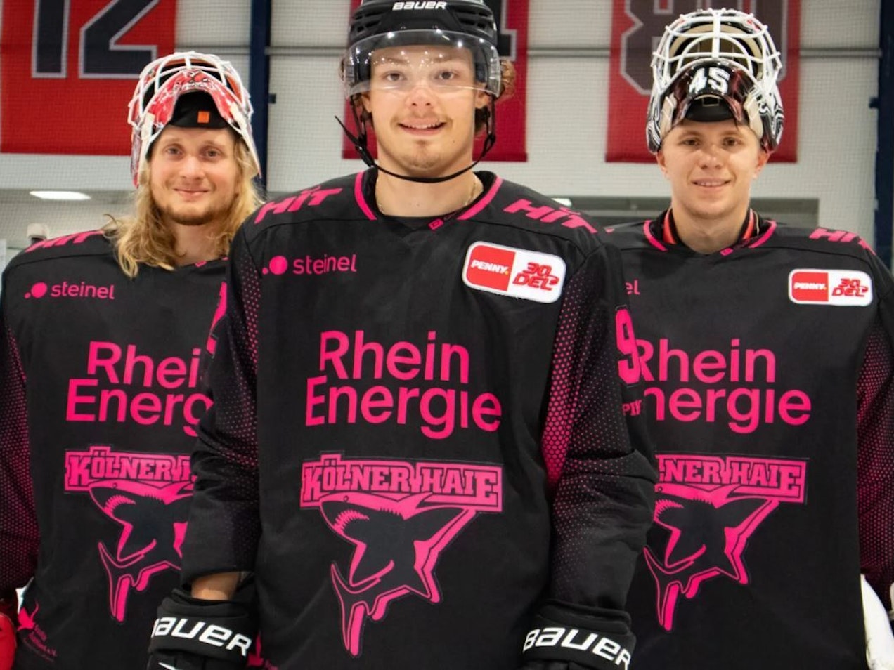 Die Pinktober-Trikots der Kölner Haie, präsentiert von Hänelt (Mitte), Pantkowski (l.) und Ancicka (r.).