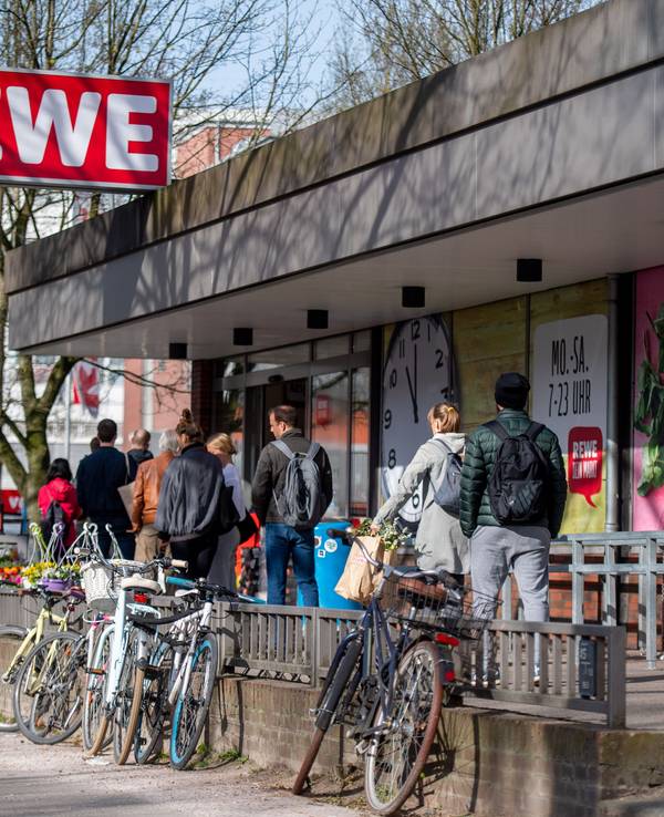 Menschen warten in einer Schlange vor einem Rewe Markt.