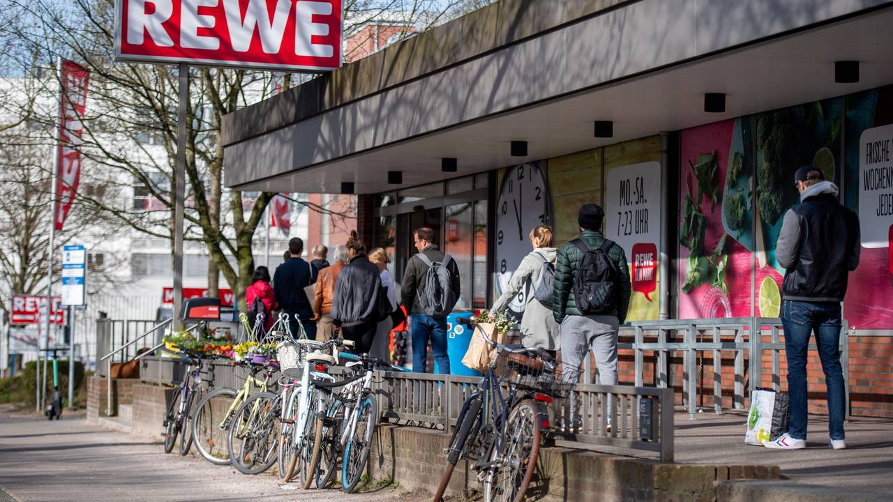 Menschen warten in einer Schlange vor einem Rewe Markt.