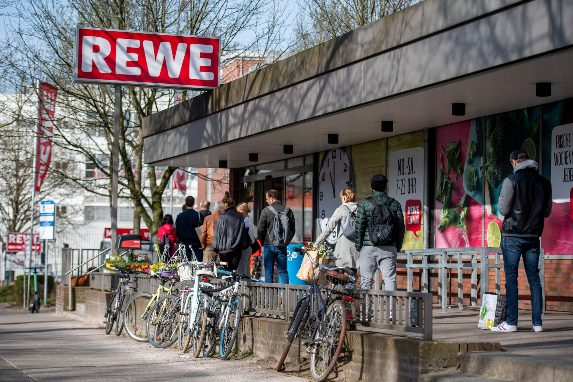 Menschen warten in einer Schlange vor einem Rewe Markt.
