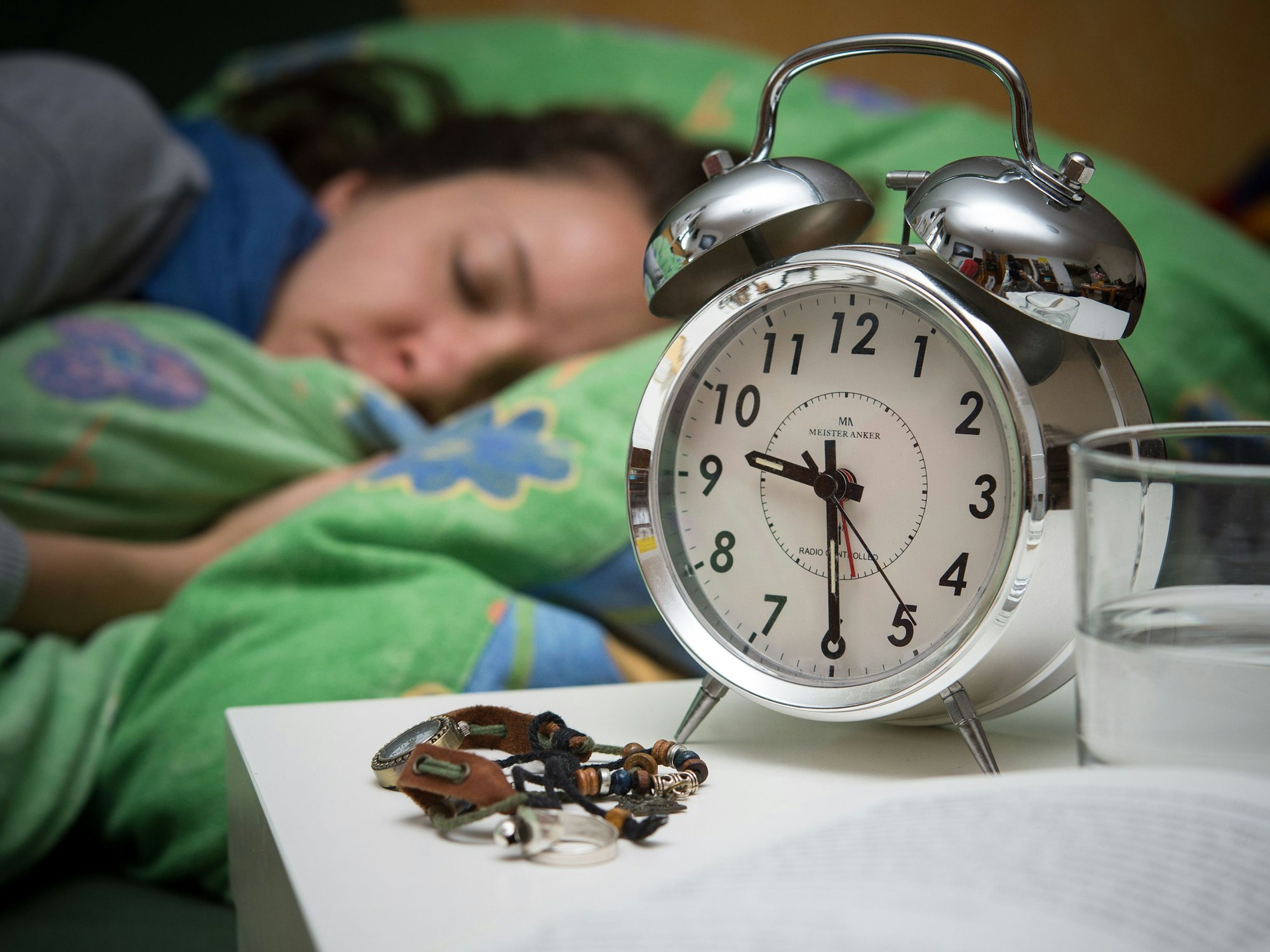 Eine Frau schläft im Bett, während ein Wecker, Wasserglas, Schmuck und ein Buch vor ihr auf dem Nachtschränkchen zu sehen sind, hier im März 2016 in Brandenburg.