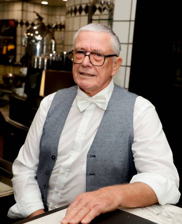 Rainer Diederichs steht in seinem Bistro und lächelt fein gekleidet in die Kamera.