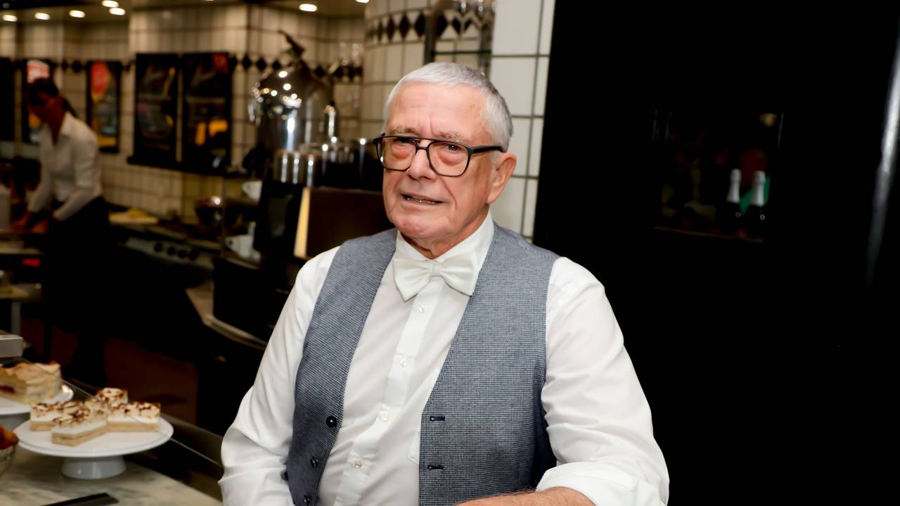 Rainer Diederichs steht in seinem Bistro und lächelt fein gekleidet in die Kamera.