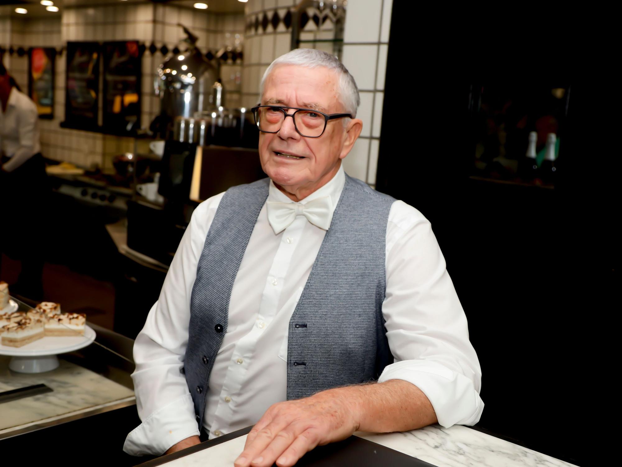 Rainer Diederichs steht in seinem Bistro und lächelt fein gekleidet in die Kamera.