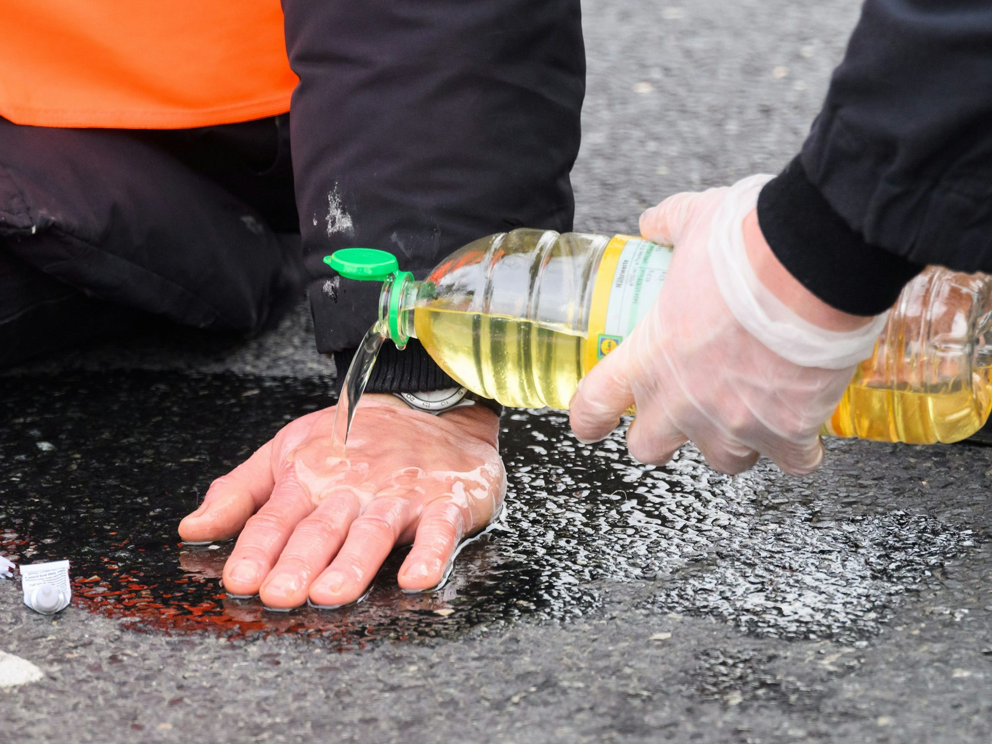 Polizisten versuchen, festgeklebte Hände von Aktivisten der Gruppierung „Letzte Generation“ mit Speiseöl von der Straße zu befreien.