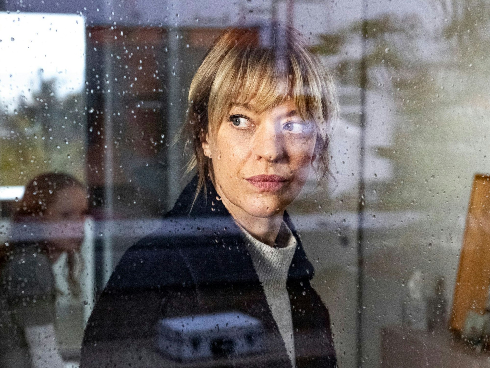 Ellen Berlinger (Heike Makatsch) schaut durch ein Fenster, auf dem Regentropfen zu sehen sind.