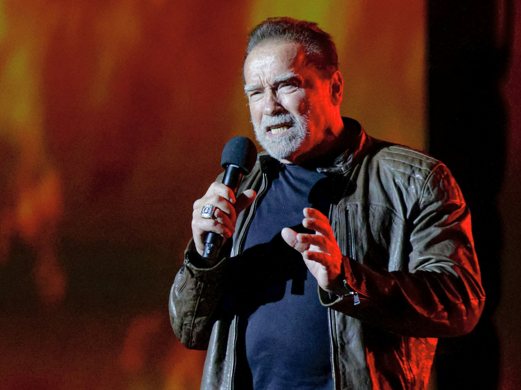 Arnold Schwarzenegger spricht in ein Mikrofon. Er trägt eine Lederjacke.