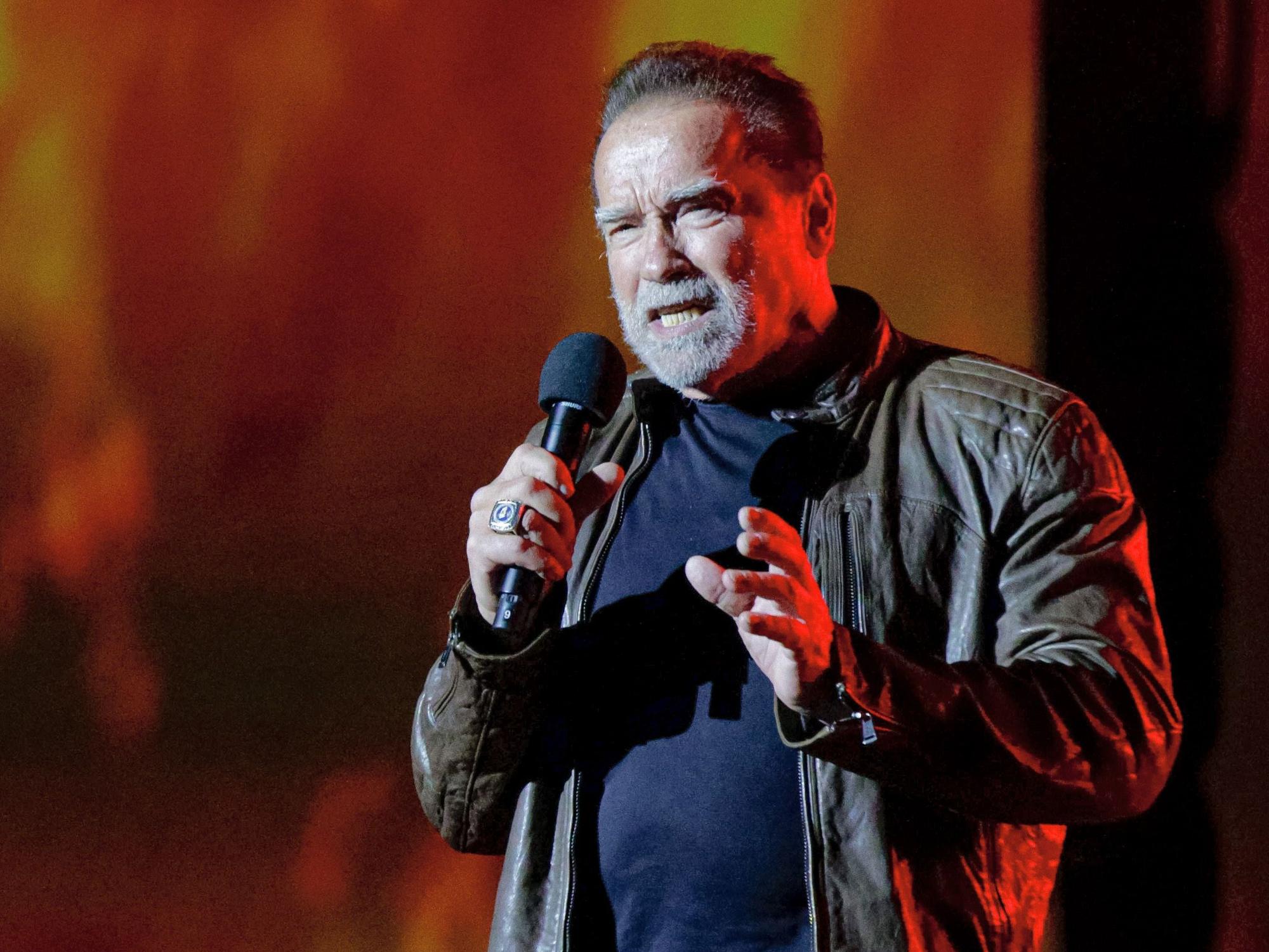 Arnold Schwarzenegger spricht in ein Mikrofon. Er trägt eine Lederjacke.