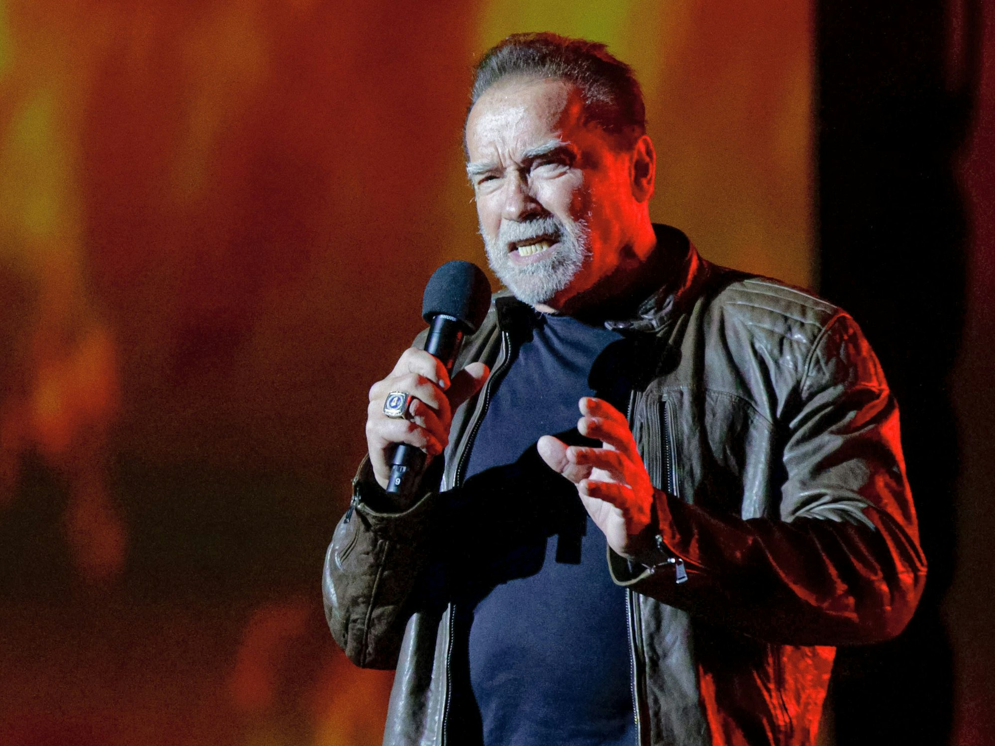 Arnold Schwarzenegger spricht in ein Mikrofon. Er trägt eine Lederjacke.