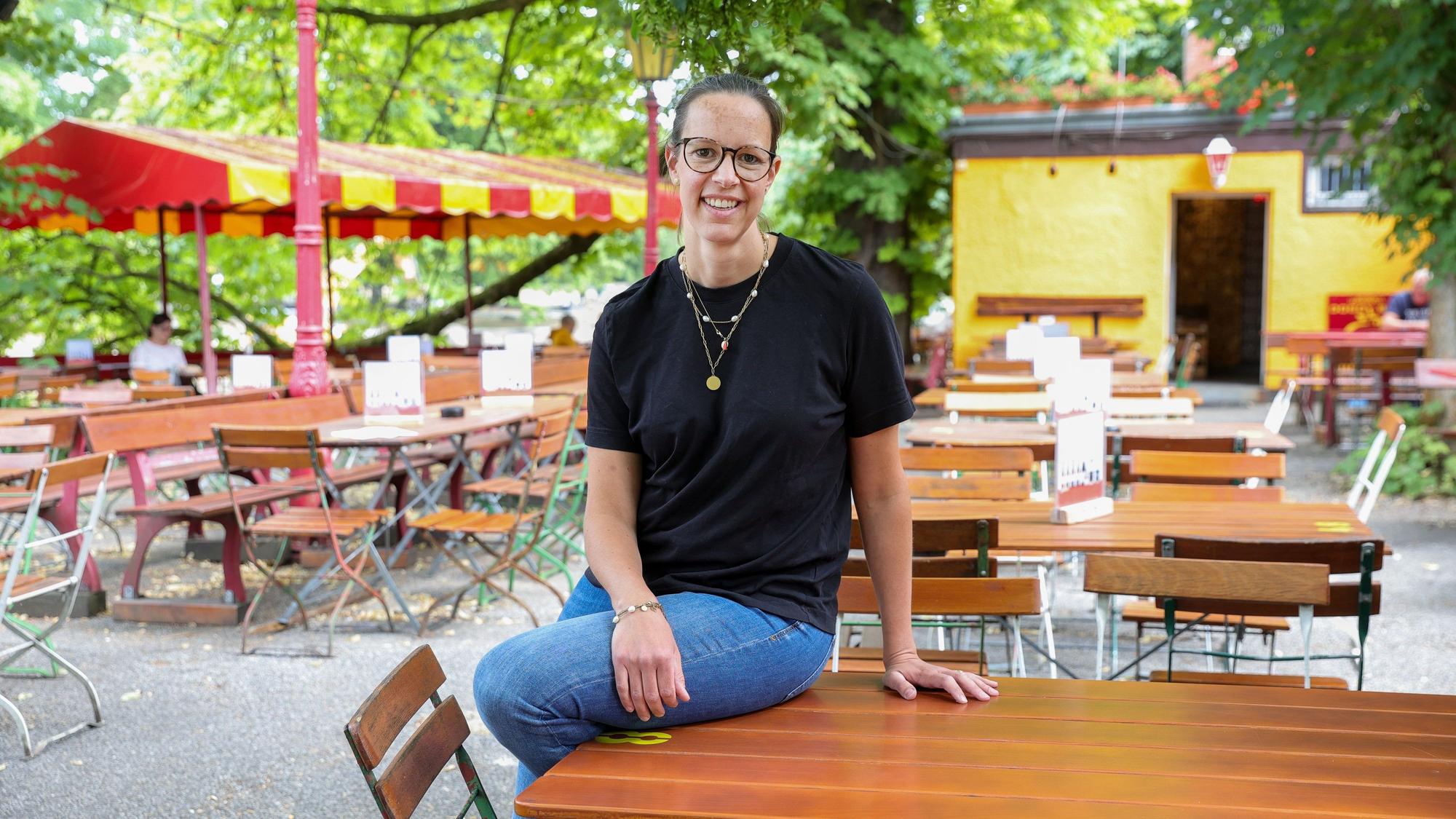 Die Kölner Gastronomin Anna Heller sitzt an einem Tisch in ihrem Biergarten im Kölner Volksgarten und schaut in die Kamera.