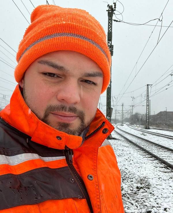 Ein Mann steht im Winter an Bahngleisen.