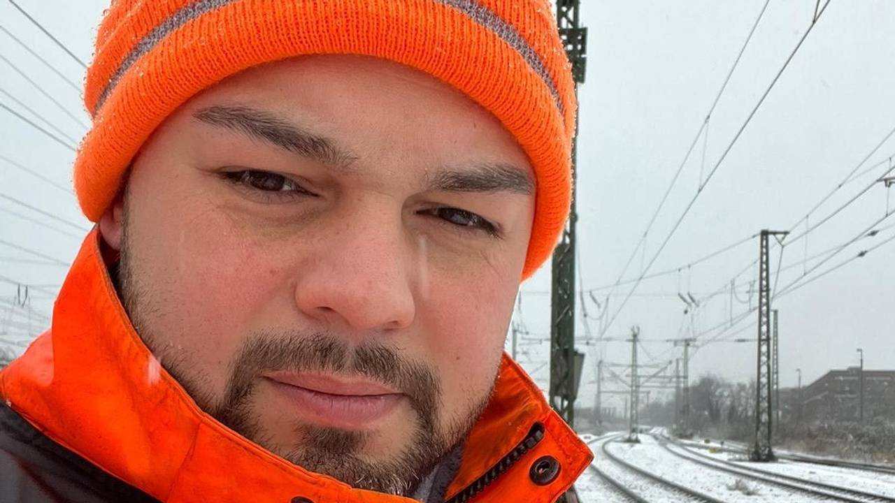 Ein Mann steht im Winter an Bahngleisen.