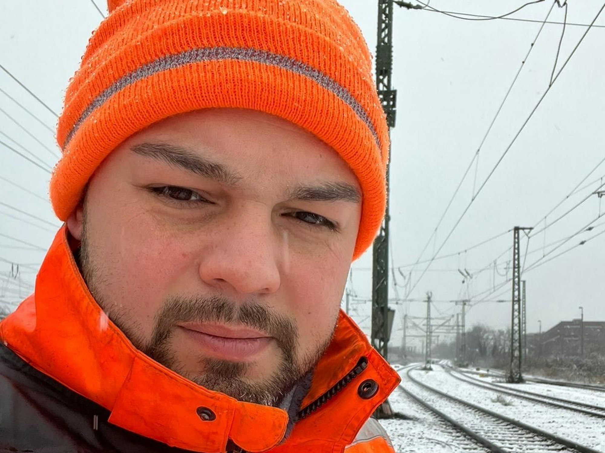 Ein Mann steht im Winter an Bahngleisen.