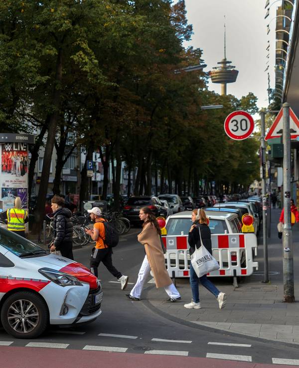 Ein Autos des Ordnungsamts sperrt eine Straße ab, Menschen gehen zu Fuß vorbei.